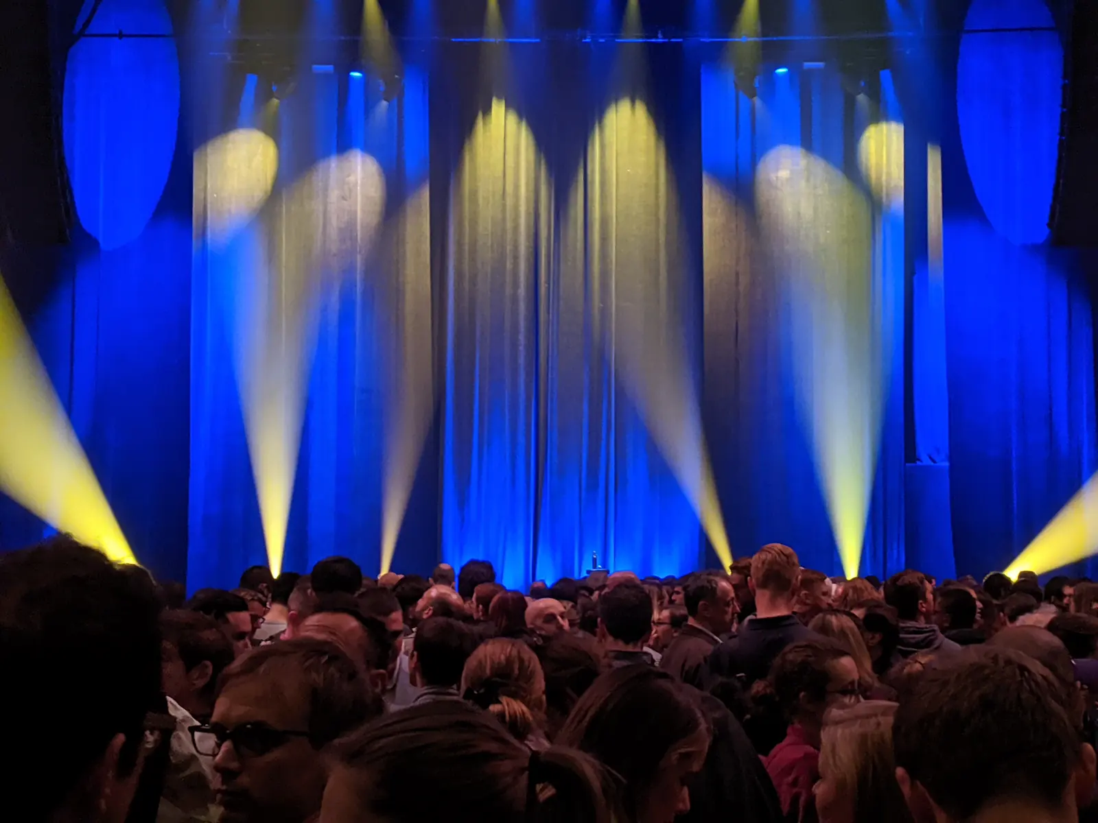 A packed crowd waiting under blue and gold stage lights before a show